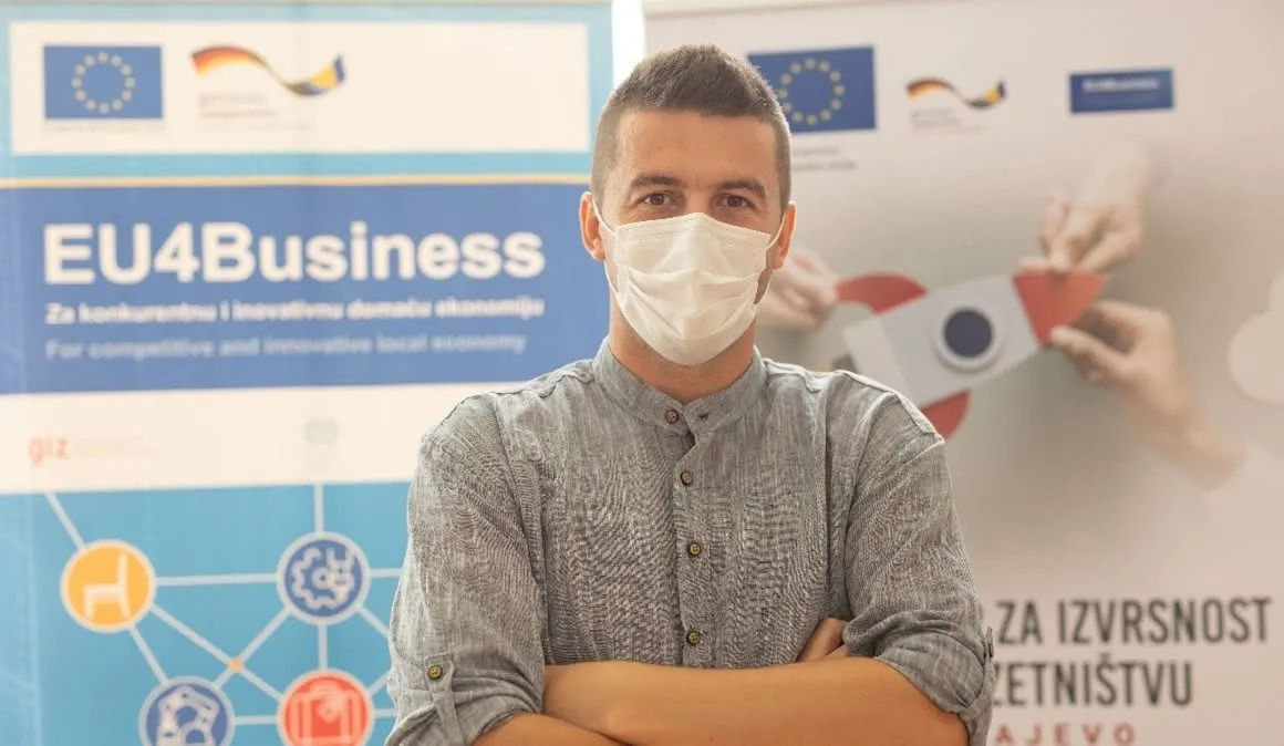 Amer Skrobo stoji prekrštenih ruku, sa maskom na licu, ispred bannera EU4Business i Centra za izvrsnost u poduzetništvu Sarajevo.